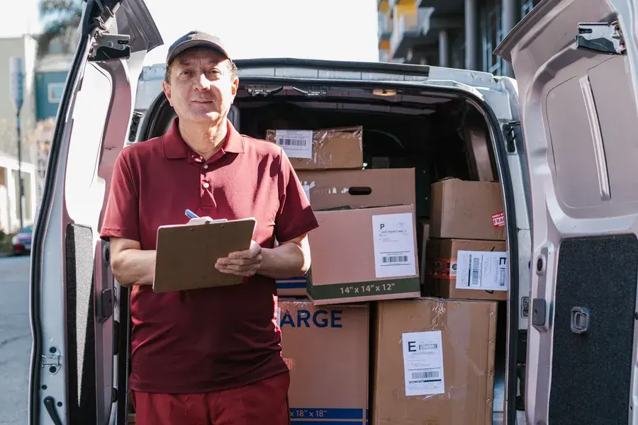 Courier writing on a clipboard in front of a van loaded with parcels