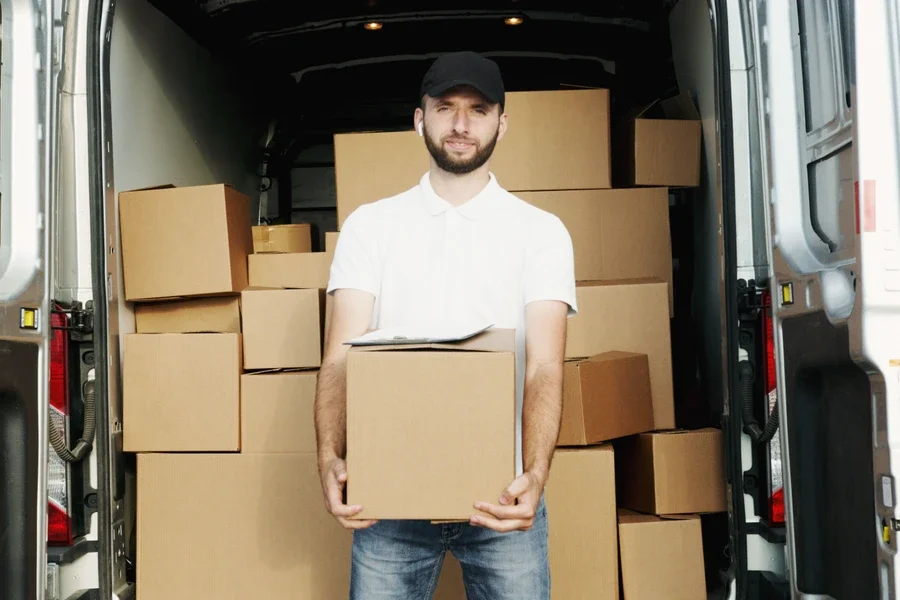 Courier holding a parcel at the open rear doors of a van full of boxes