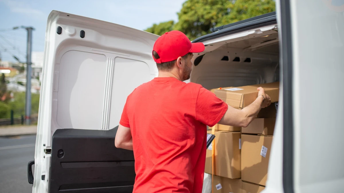 Courier in a red cap and T-shirt loading parcels into the back of a white van