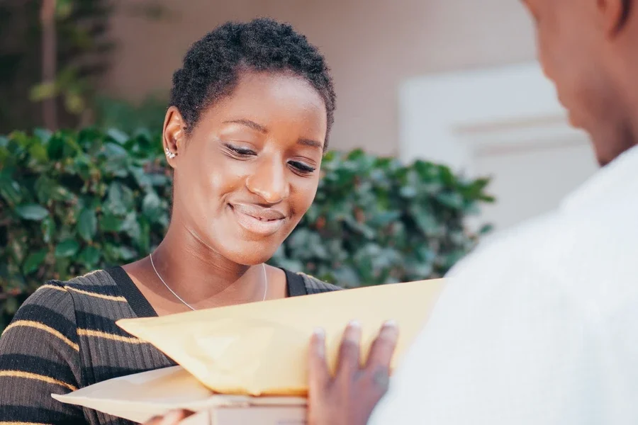 Smiling customer receiving padded envelopes from a courier at her front door