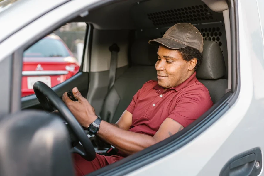 Delivery driver in a red polo checking his phone behind the wheel of a white van