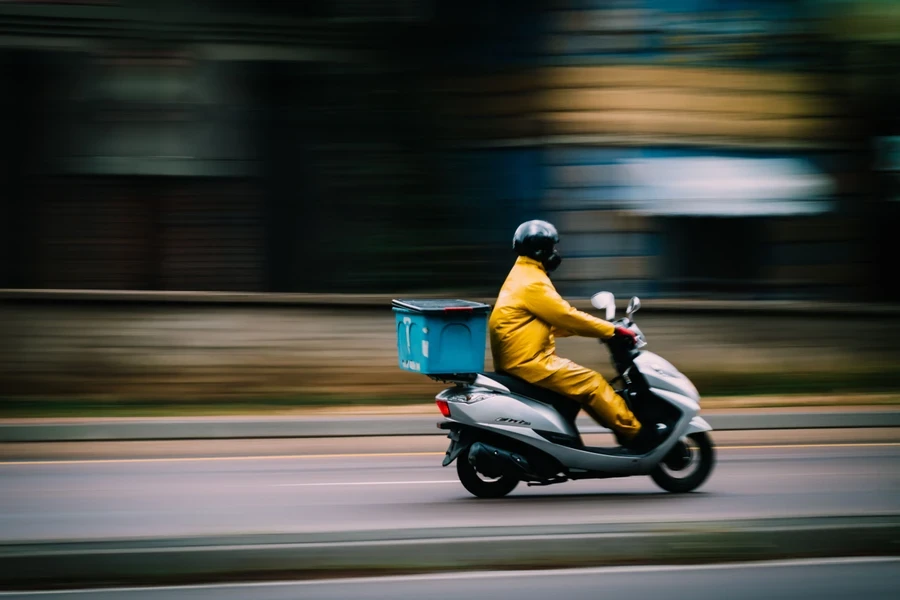 Delivery rider on a scooter with a courier box on the back riding along a road