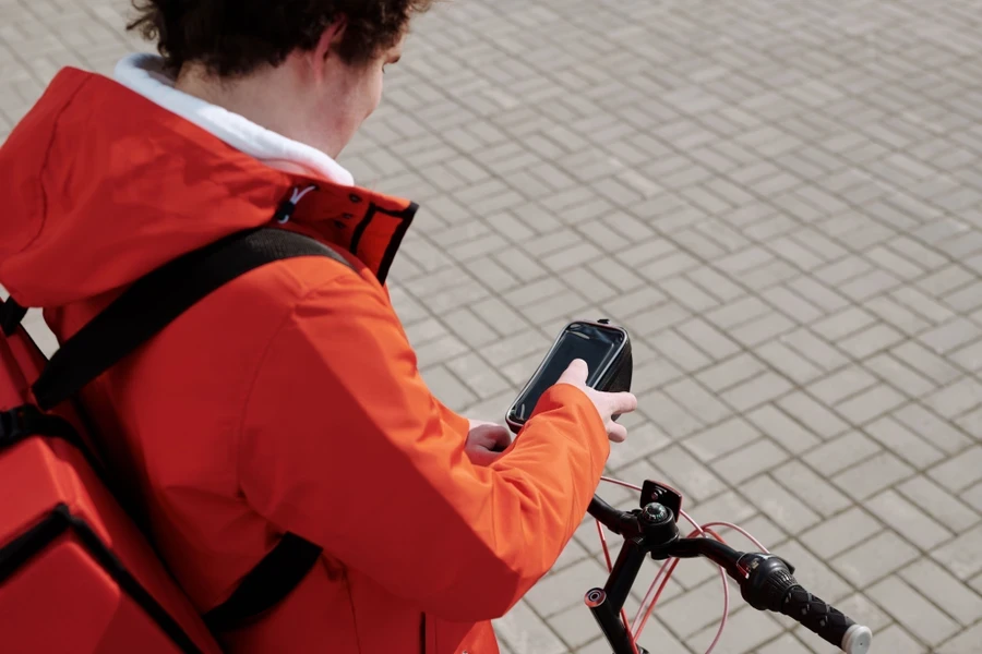 Bicycle courier in a red jacket with a thermal backpack checking his phone