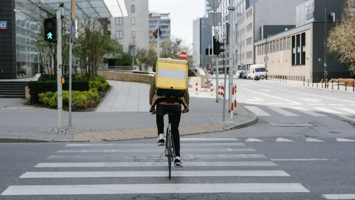 Food delivery cyclist with a yellow thermal backpack crossing a city street