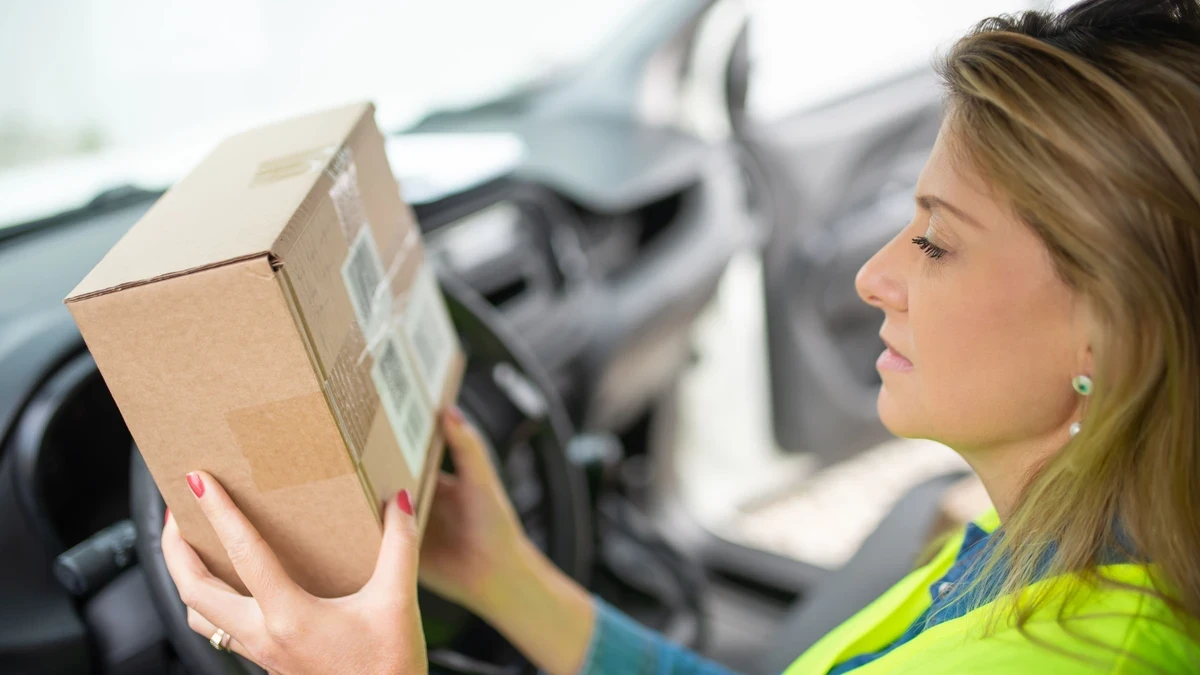Delivery driver in a hi-vis vest checking the label on a parcel while sitting behind the wheel of her car