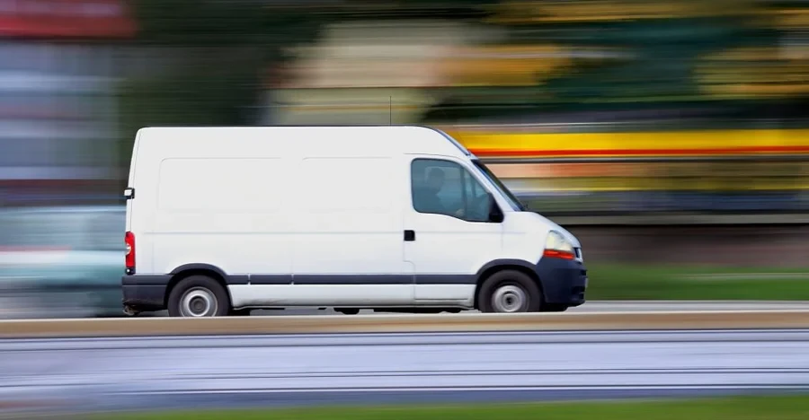 White delivery van driving at speed past a blurred roadside