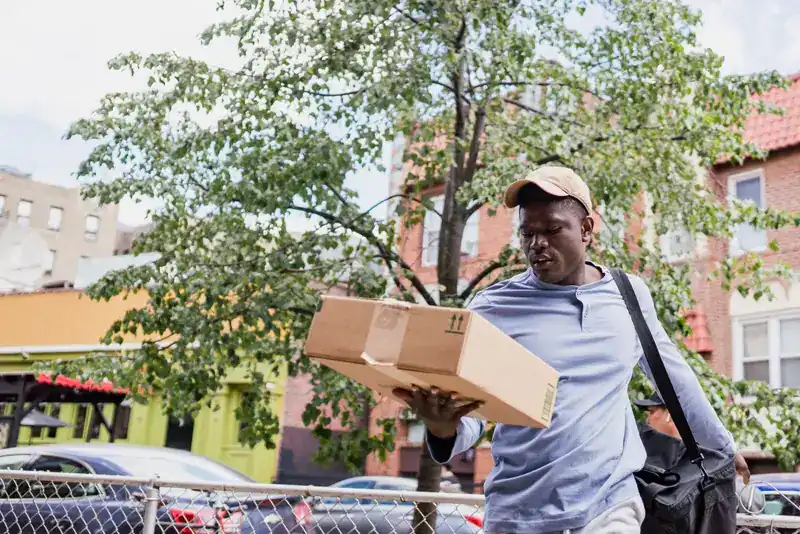 Courier carrying a cardboard parcel along a city street between drops