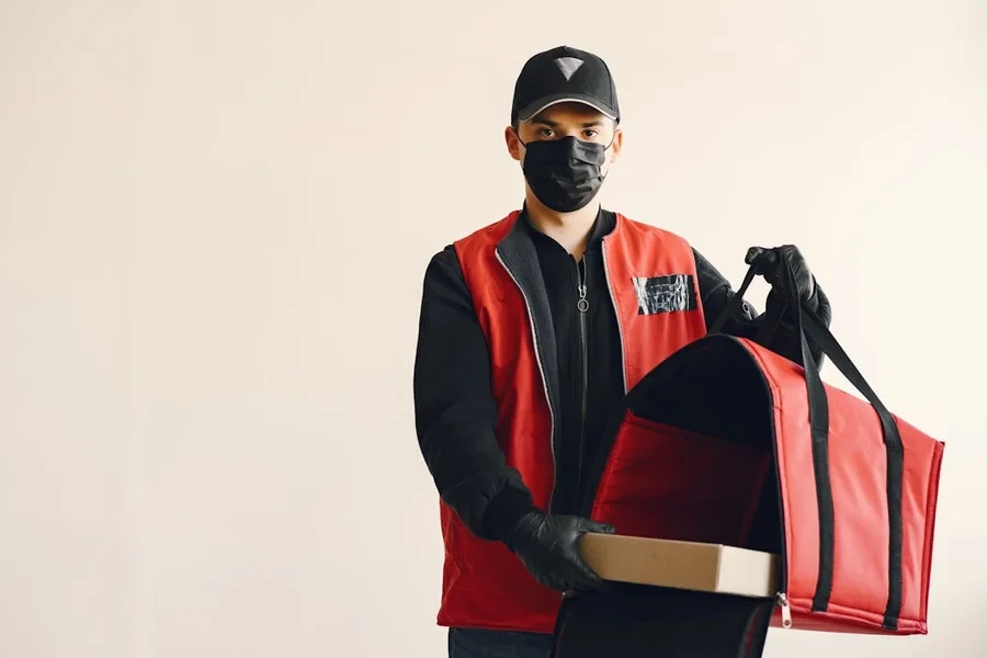 Courier in a red vest holding an insulated delivery bag and a pizza box