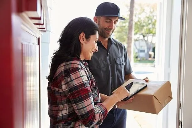Courier at a front door handing a parcel to a customer who signs for it on a tablet