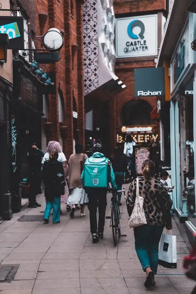 Deliveroo cyclist with a teal thermal backpack riding through a busy shopping street