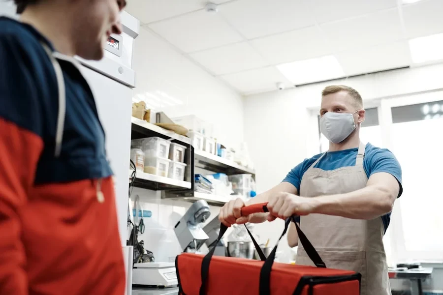 Restaurant staff handing a red thermal delivery bag to a waiting courier