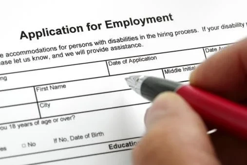 Close-up of a hand completing an application form with a pen