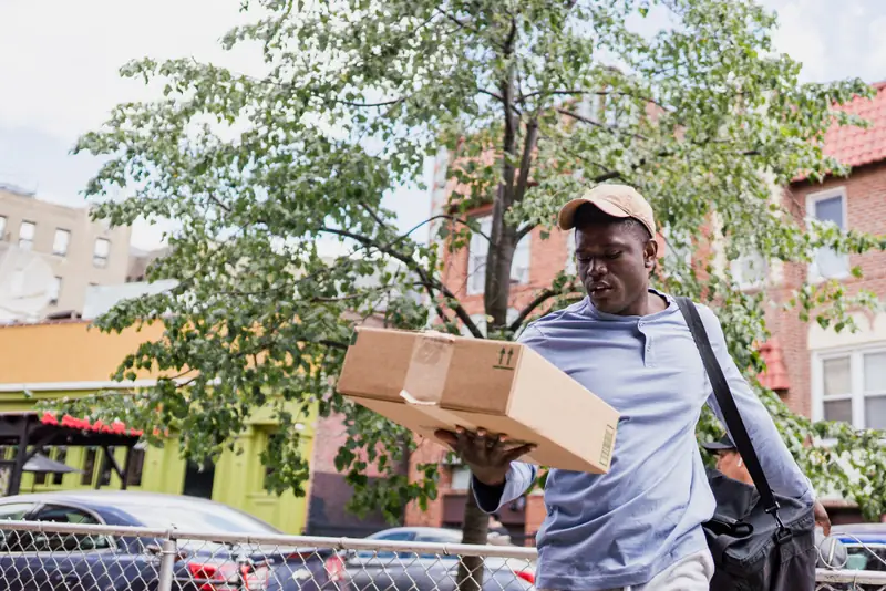 Courier carrying a cardboard parcel along a city street between drops