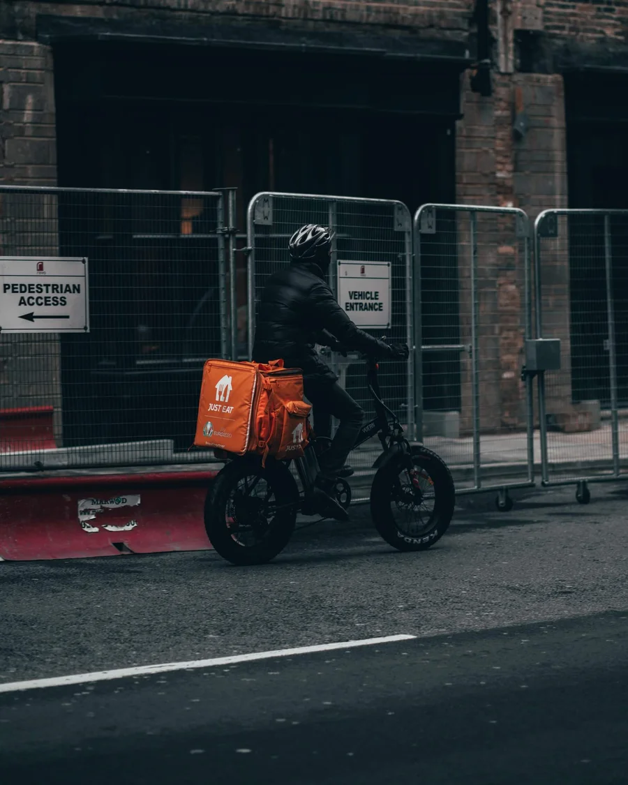 Cyclist riding an e-bike with an orange Just Eat delivery box mounted on the rear rack