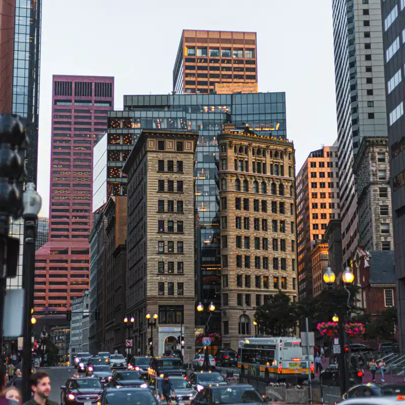 Evening rush hour traffic and an MBTA bus on a downtown Boston street lined with old stone buildings and glass towers