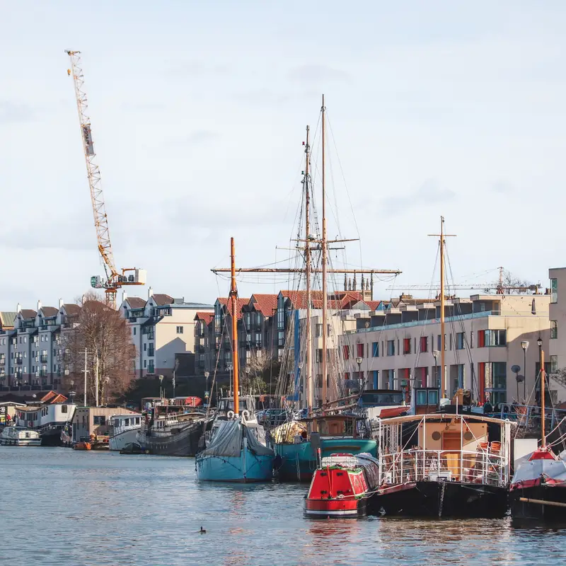 Boats and a tall ship moored in Bristol's Floating Harbour, with flats along the waterside and a construction crane behind