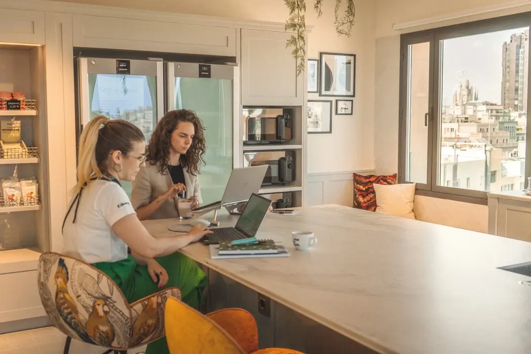 Zwei Kolleginnen arbeiten mit Laptops an der Kücheninsel, daneben ein Fenster mit Blick über die Stadt