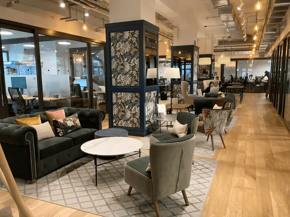 Offene Lounge mit Sofas, Sesseln und einer gemusterten Säule, dahinter der Bereich mit den Schreibtischen