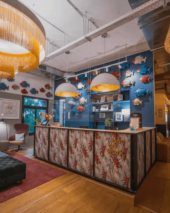 Empfang des Büros von Service Club mit gemustertem Tresen, Pendelleuchten und Keramikfischen an einer blauen Wand