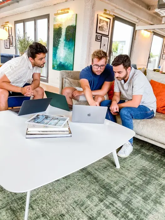 Drei Kollegen arbeiten gemeinsam mit Laptops auf den Sofas der Lounge