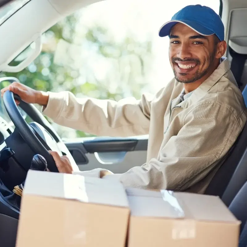 Smiling delivery driver gripping the steering wheel with cardboard packages on the passenger seat