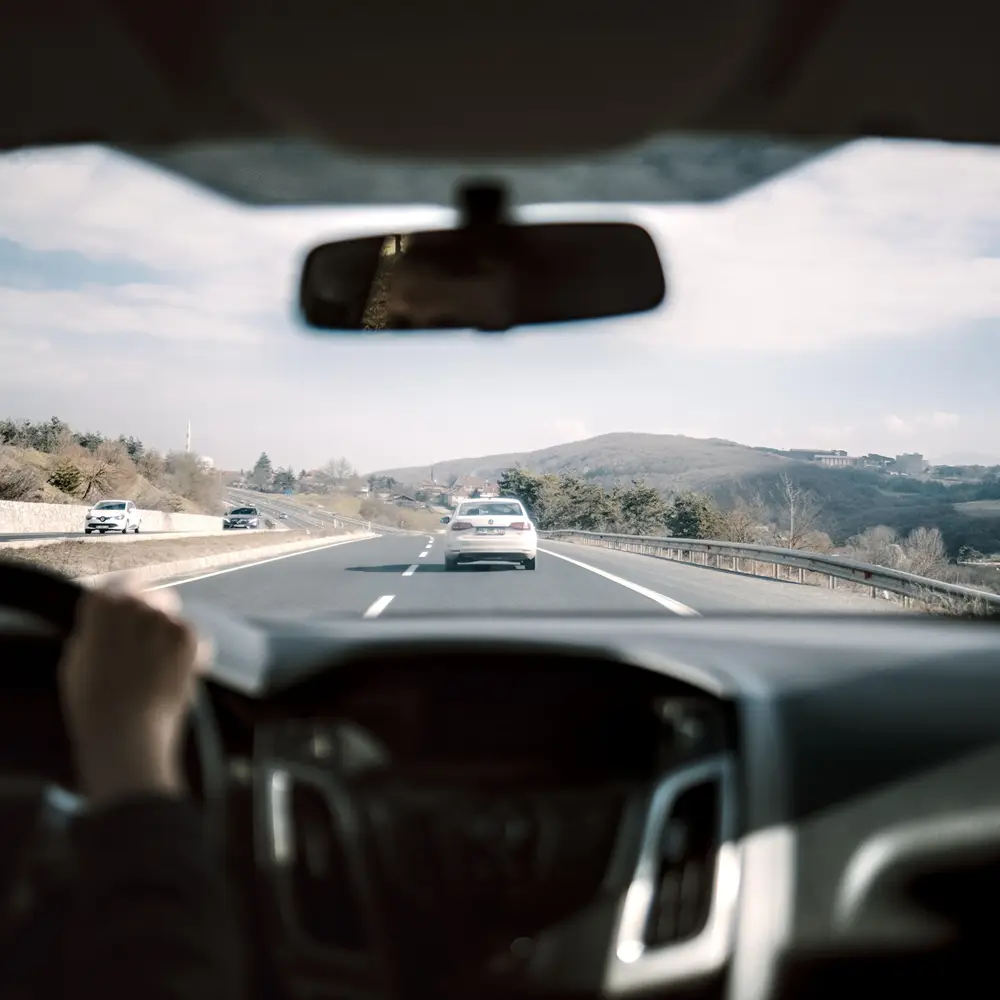 The view through a windshield on an open highway, hands on the wheel