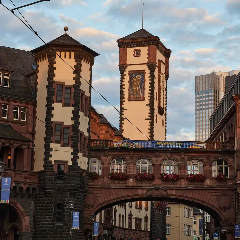 Die Türme des Frankfurter Rathauses mit der überdachten Brücke über die Straße, dahinter ein Hochhaus der Skyline