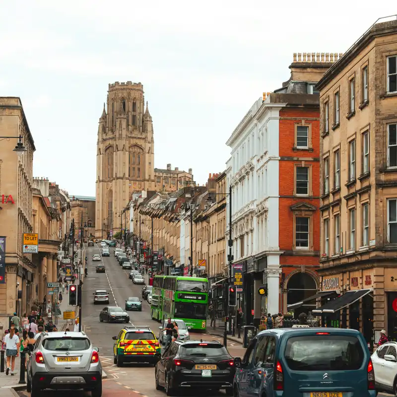 Traffic on Park Street in Bristol, with a green double decker bus, an ambulance and cars climbing towards the Wills Memorial Building tower