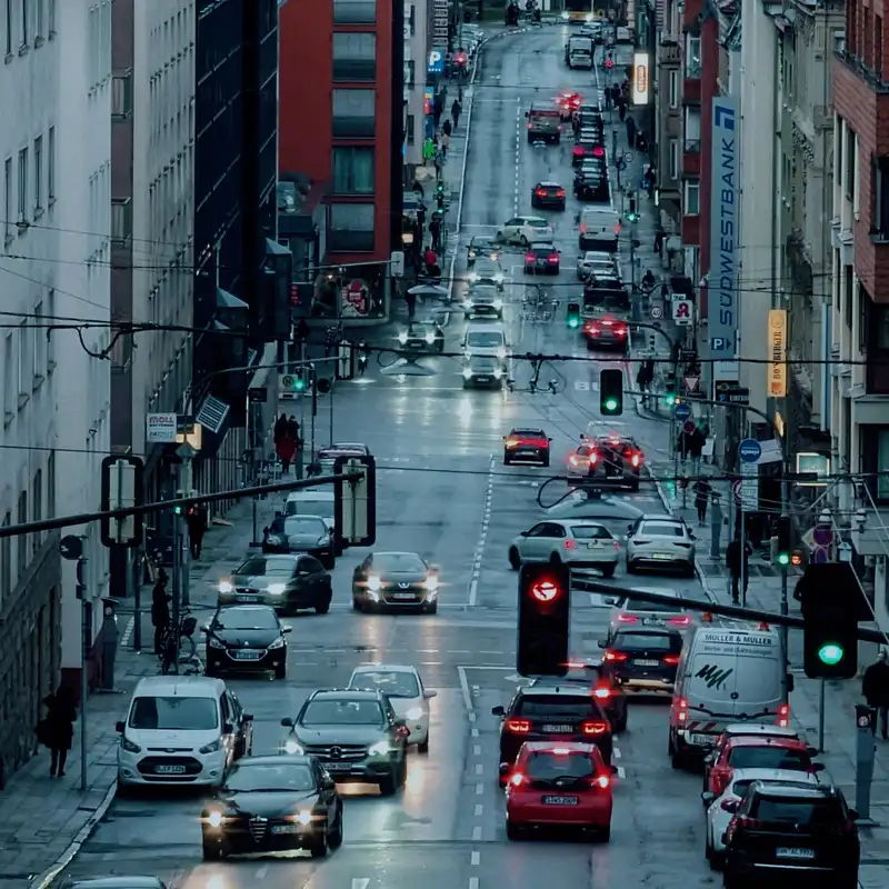 Blick von oben auf eine belebte Straße in Stuttgart in der Dämmerung, mit dichtem Autoverkehr, weißen Transportern und Ampeln, im Hintergrund Häuser am Hang
