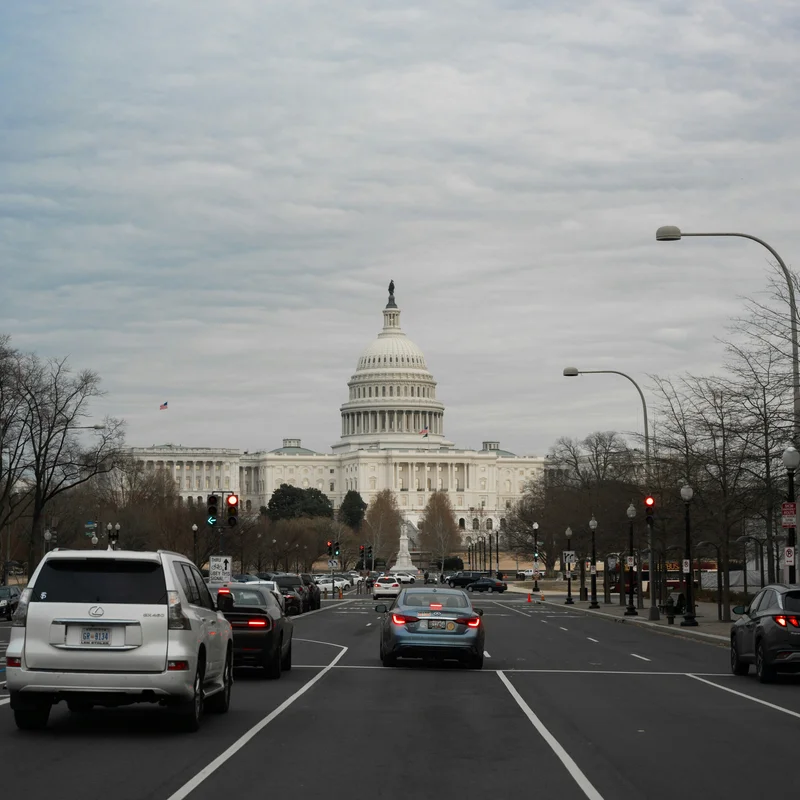 Cars driving up a wide avenue toward the United States Capitol under a gray sky