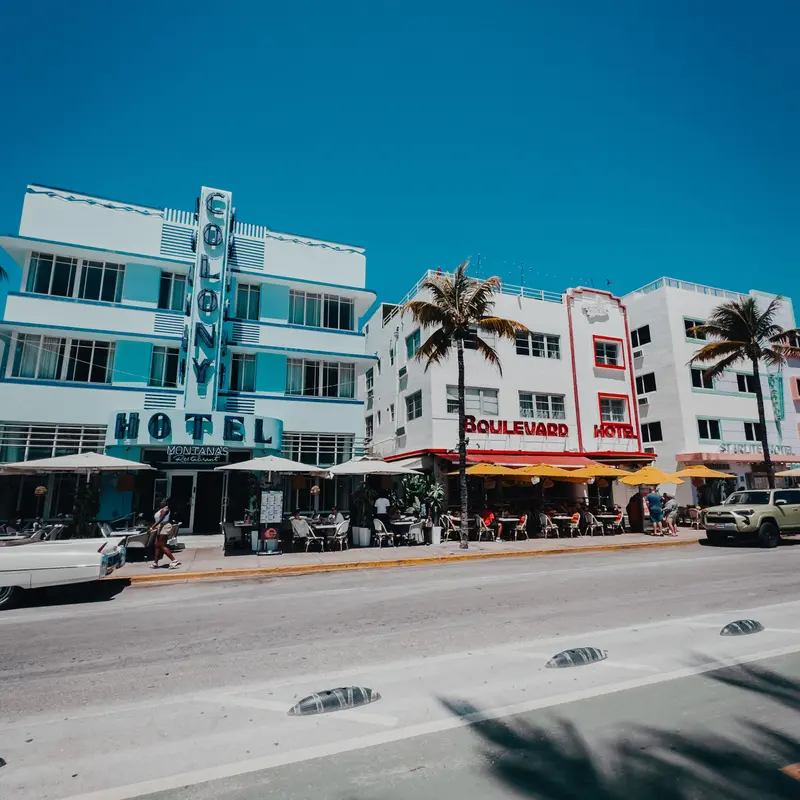 Art Deco hotels with sidewalk cafes and yellow umbrellas along Ocean Drive in South Beach, under a clear blue sky