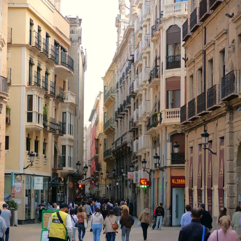 Calle peatonal del centro histórico de Murcia llena de gente, entre edificios de balcones de hierro y farolas