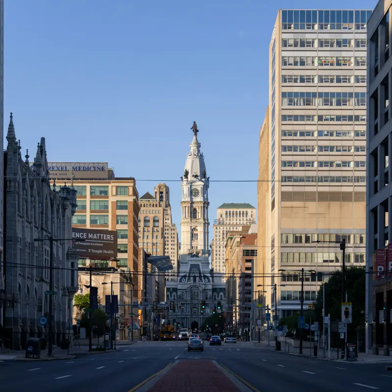 Broad Street running straight toward the clock tower of Philadelphia City Hall, with office towers on both sides and light morning traffic