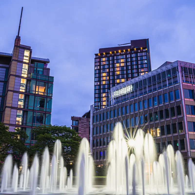 Fountains lit up at dusk in Sheffield city centre, in front of glass office blocks and a tall tower
