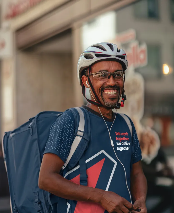 A smiling cycle courier in a Service Club jersey with a delivery backpack