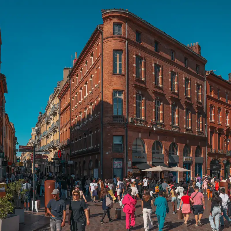 Une foule de piétons dans une rue du centre de Toulouse, devant un immeuble d'angle en brique rose